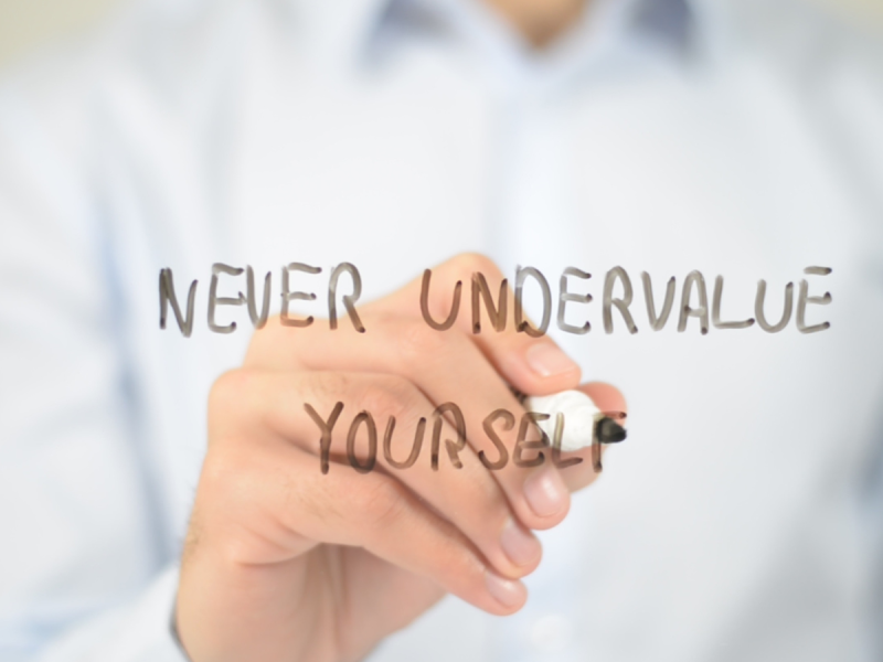 A hand writing the word Never Undervalue Yourself